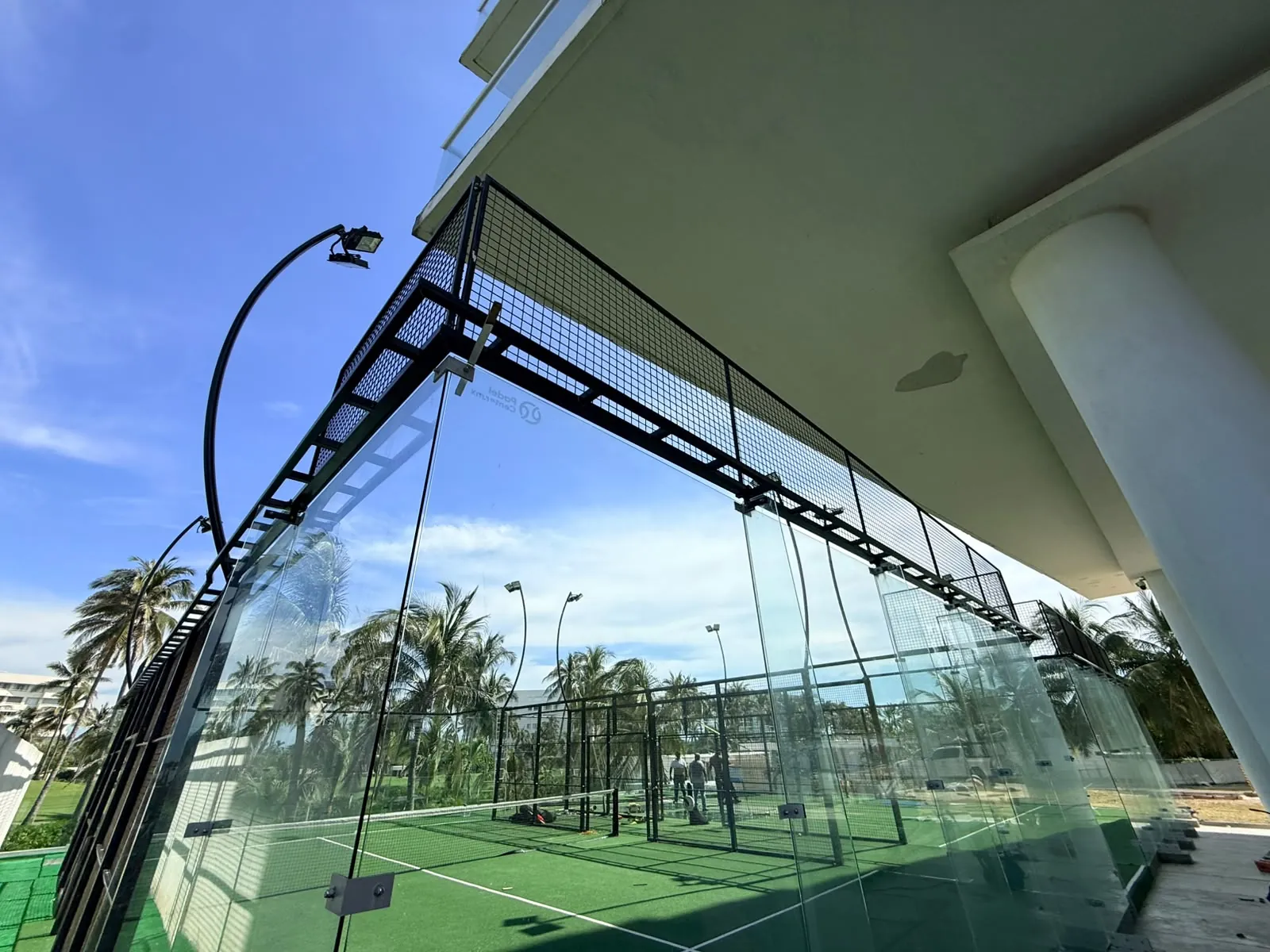 Esquina de una cancha de pádel con cinturón perimetral, cristales templados y malla bajo un edificio en Acapulco