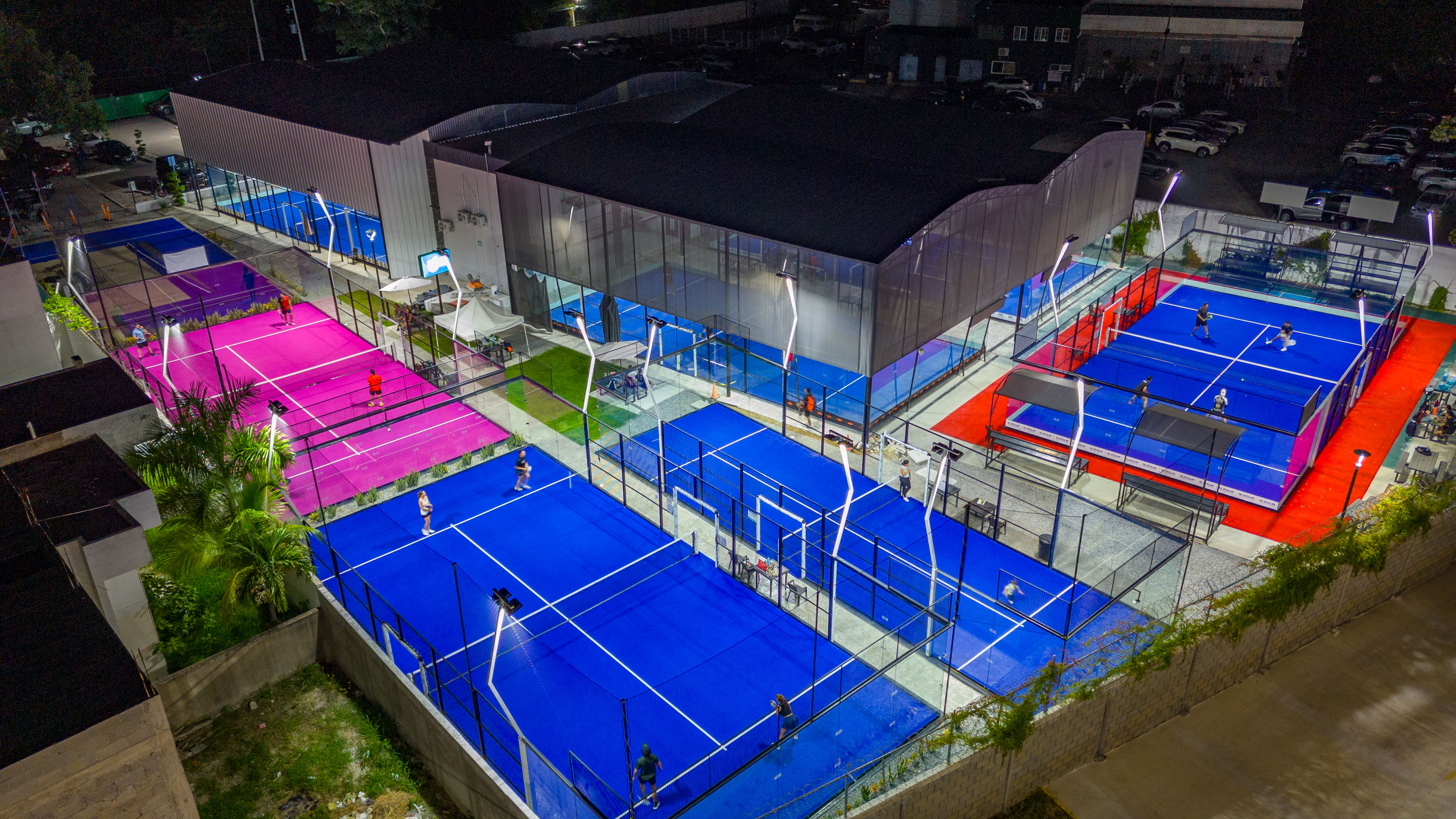 Club de pádel multicancha nocturno con canchas azules y rosas en operación