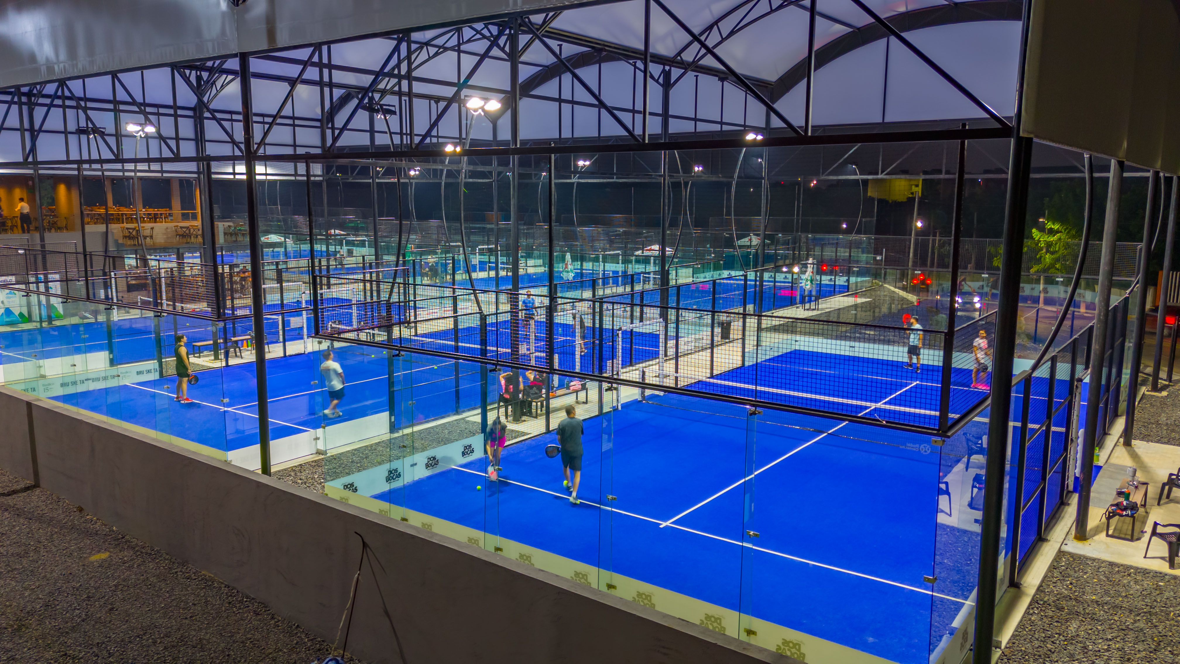 Club de pádel techado con varias canchas azules e iluminación nocturna