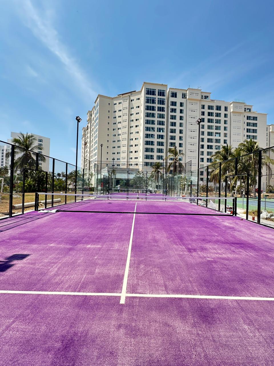 Desarrollo Acapulco — cancha de pádel pasto morado con torres de condominios al fondo PadelCenter